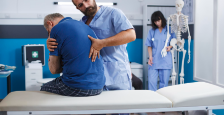 Clinician supports a patient during an examination on an exam table, with a skeleton model and staff in the background.